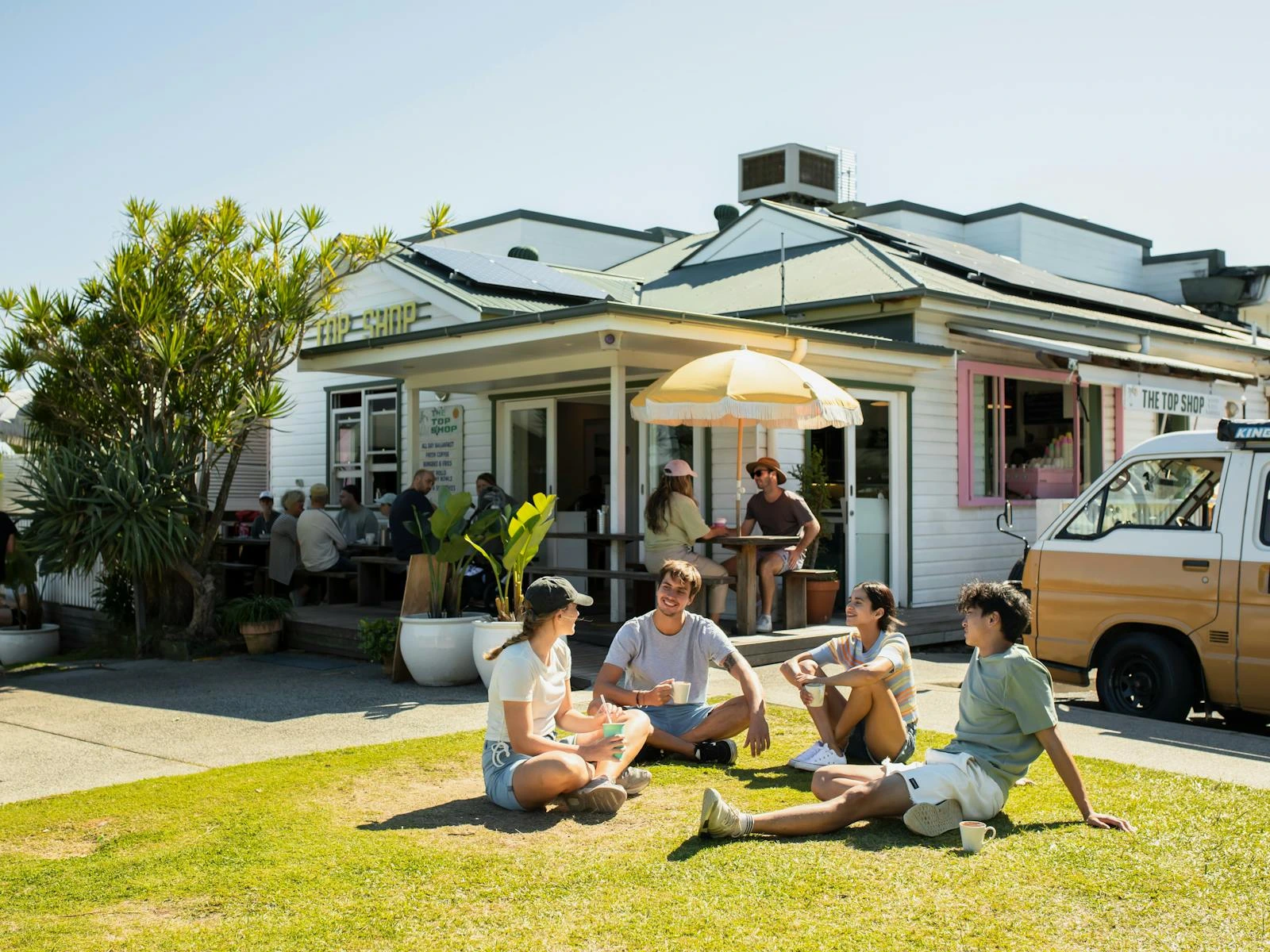 Four people sitting on the grass outside The Top Shop cafe in Byron Bay.